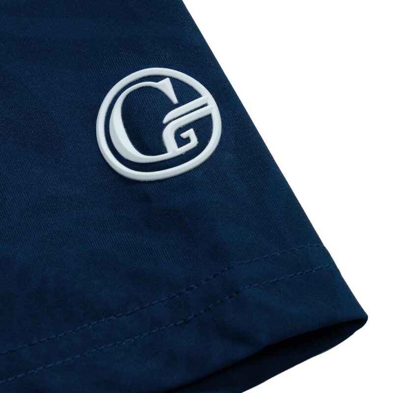 Close-up of navy fabric with a white embroidered circular G logo near the hem of a sleeve.